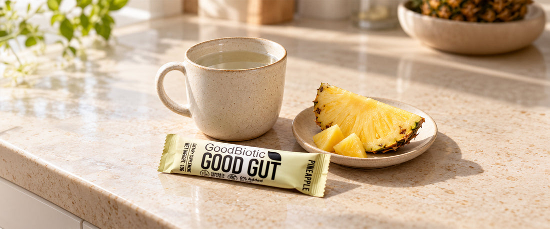 A morning kitchen scene in soft light with a cup of warm water, a slice of pineapple on a small plate, and a GoodGut sachet resting beside them.