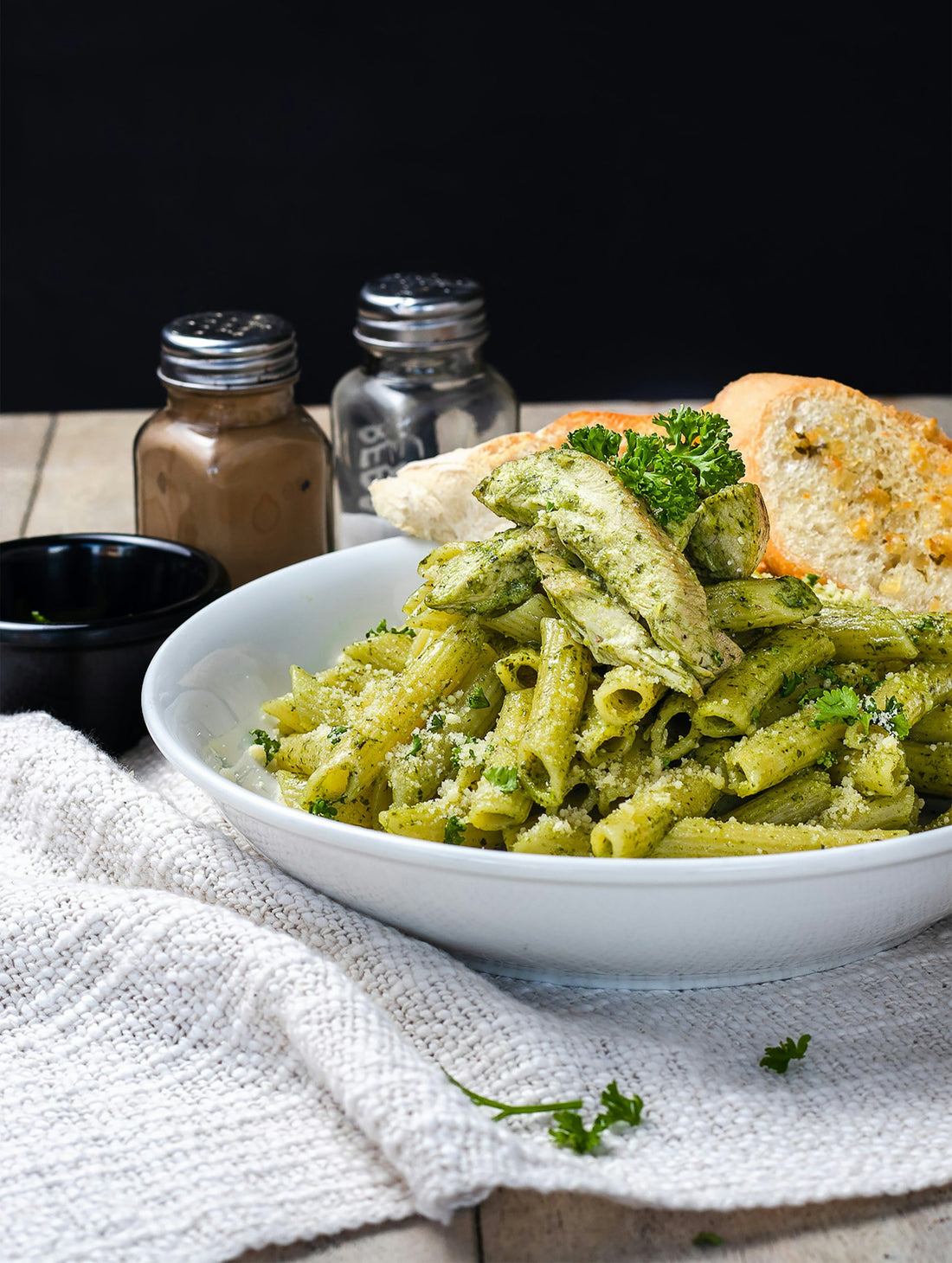Bowl of penne pasta tossed in green pesto with herbs and bread, a quick high-protein weeknight dinner