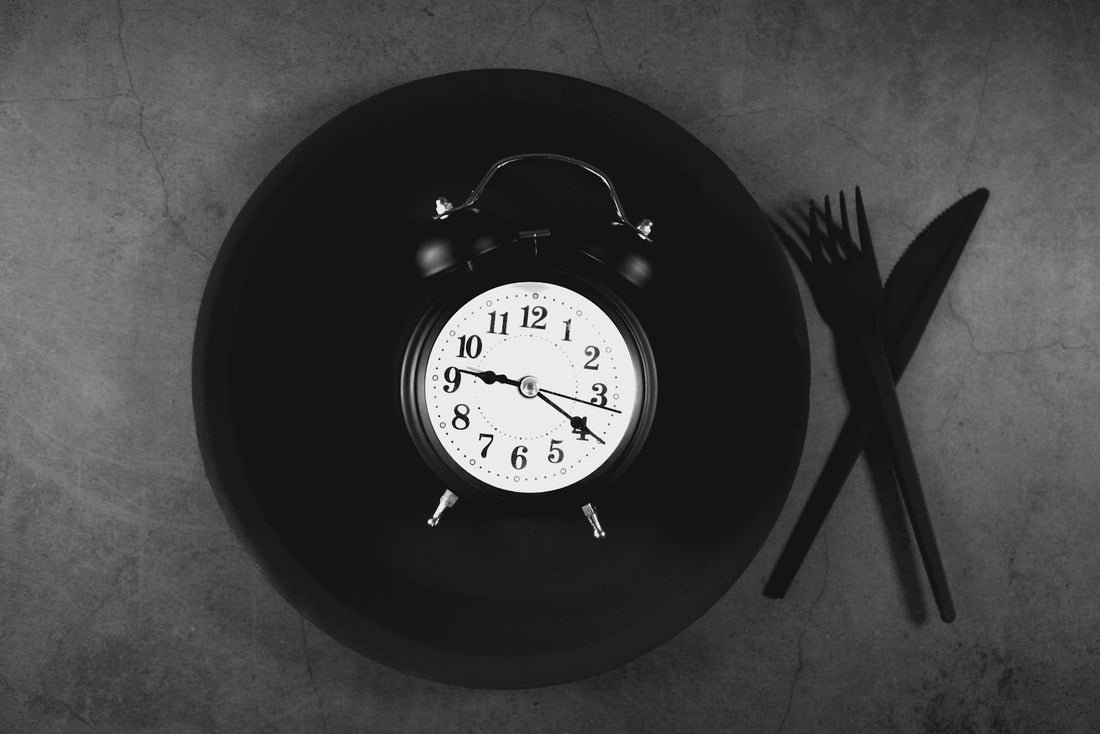 Alarm clock on an empty dinner plate with a fork and knife, illustrating late dinner meal timing