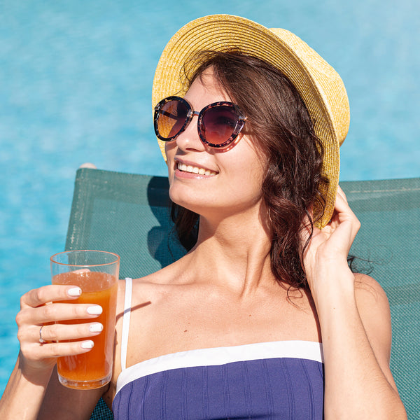 Woman in sunglasses drinking GoodGut Pineapple by a pool