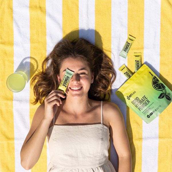 Smiling woman holding a GoodHydrate Lemon Mint sachet, packs beside her